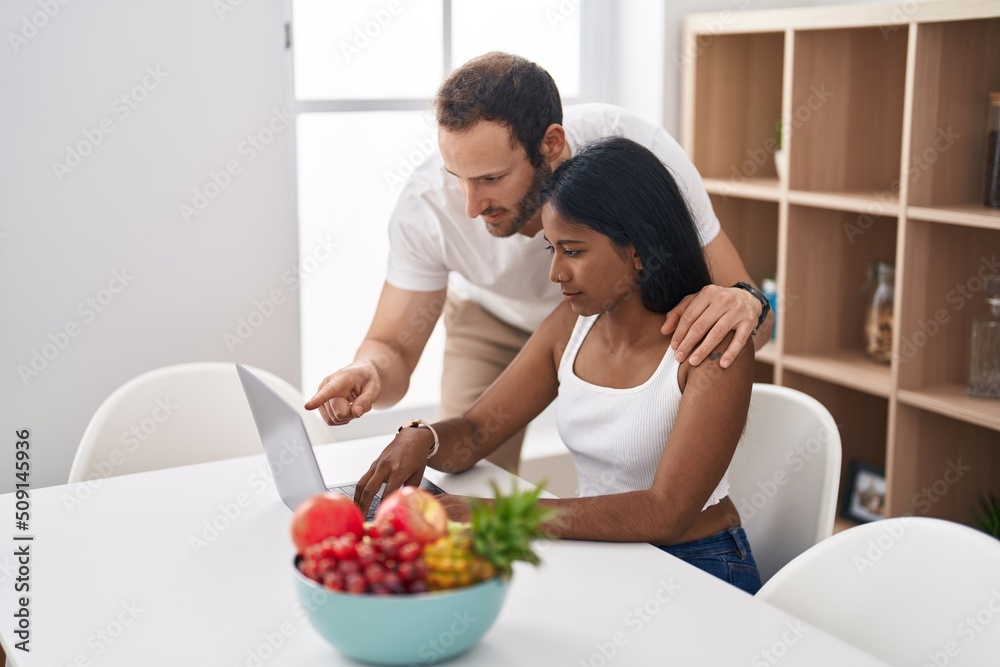 Man and woman interracial couple using laptop sitting on table at home Man and woman interracial couple using laptop sitting on table at home