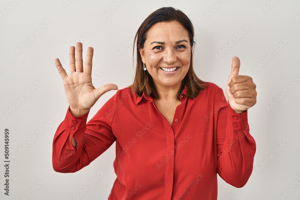 Hispanic mature woman standing over white background showing and pointing up with fingers number six while smiling confident and happy. Hispanic mature woman standing over white background showing and pointing up with fingers number six while smiling confident and happy.