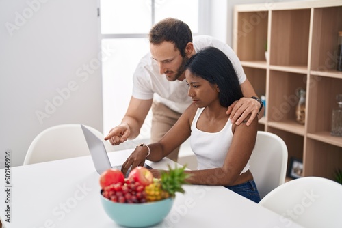 Man and woman interracial couple using laptop sitting on table at home