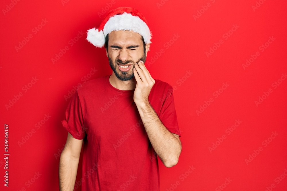 Young hispanic man wearing christmas hat touching mouth with hand with painful expression because of toothache or dental illness on teeth. dentist Young hispanic man wearing christmas hat touching mouth with hand with painful expression because of toothache or dental illness on teeth. dentist