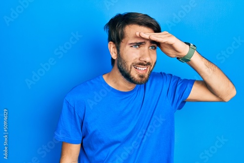 Young hispanic man wearing casual clothes very happy and smiling looking far away with hand over head. searching concept.