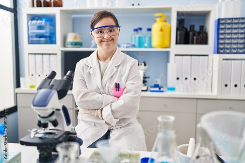 Hispanic girl with down syndrome working at scientist laboratory happy face smiling with crossed arms looking at the camera. positive person.