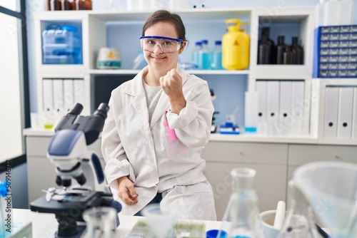 Hispanic girl with down syndrome working at scientist laboratory beckoning come here gesture with hand inviting welcoming happy and smiling