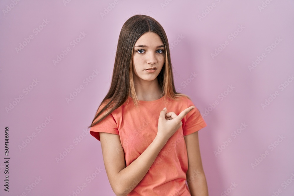 Teenager girl standing over pink background pointing aside worried and nervous with forefinger, concerned and surprised expression Teenager girl standing over pink background pointing aside worried and nervous with forefinger, concerned and surprised expression