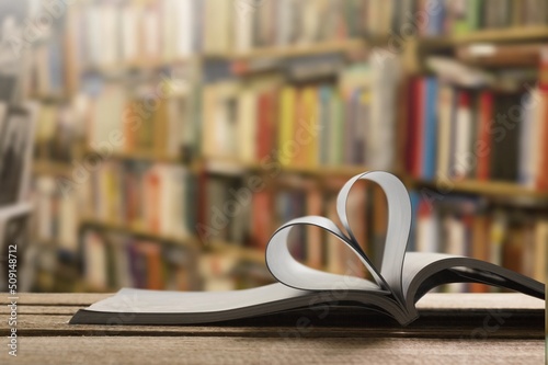 An open book forming a heart with two pages in the center, in the library. In the background are shelves full of books.