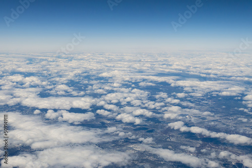 Aerial shot of snowy forested mountain tops, with stratospheric clouds