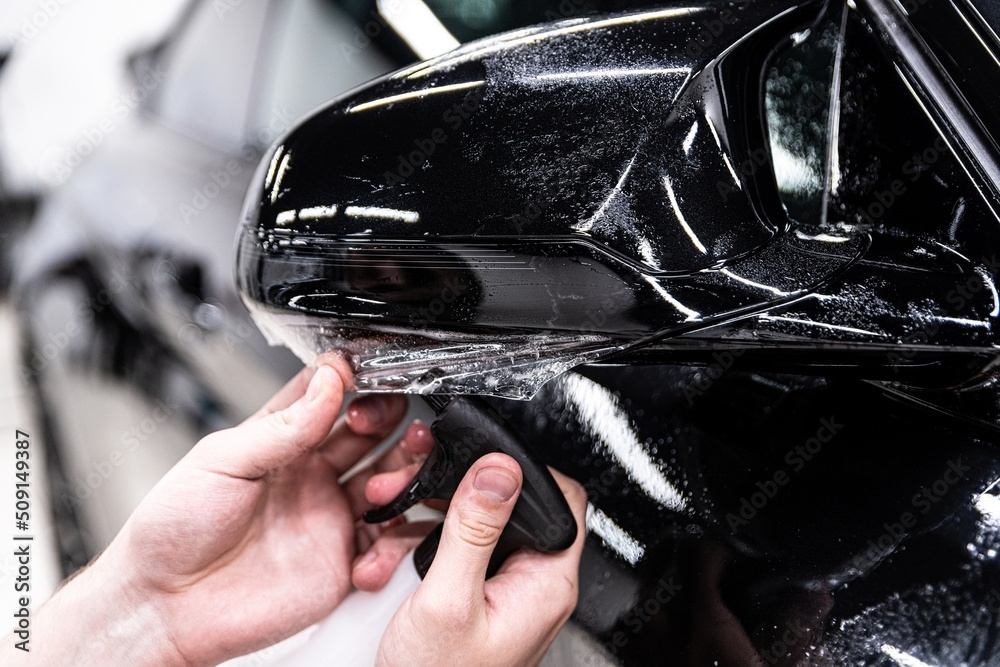 Car detailing technician applying transparent ppf foil on car body