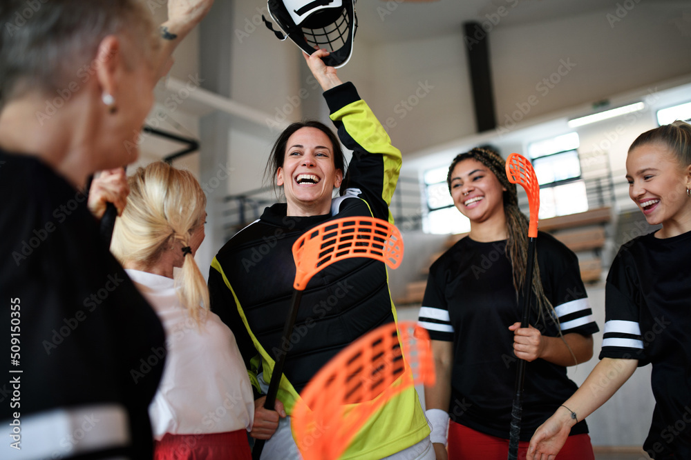 Obraz premium Group of young and old cheerful women, floorball team players, in gym cebrating victory.
