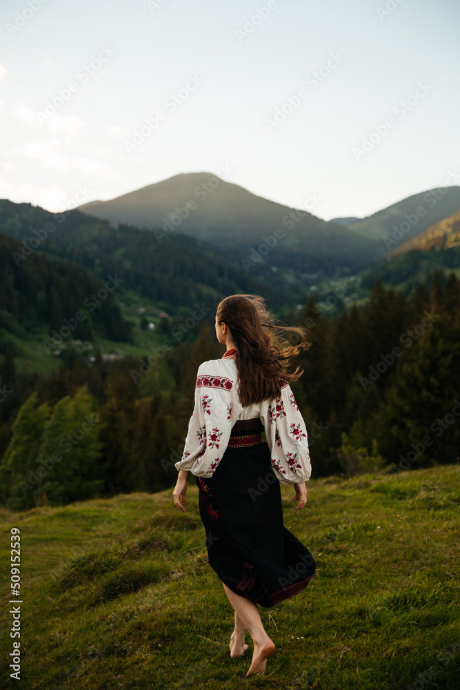 Ukrainian woman walking in Carpathians mountains in an traditional national clothing - embroidered shirt and skirt from back