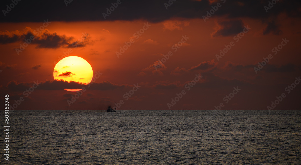 Isolated small fishing boat and the golden sunset, the fishing boat sails as the sun sets behind the clouds and the horizon. Scenic seascape photograph.