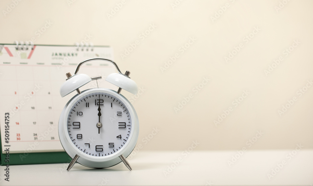 white alarm clock and the calendar on the white table, alarm clock as time passing concept for business deadline, Lunch break concept, The concept of eating on time, copy space. white alarm clock and the calendar on the white table, alarm clock as time passing concept for business deadline, Lunch break concept, The concept of eating on time, copy space.