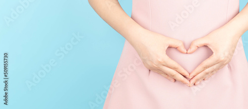 Close up of healthy woman hand made heart shape on her stomach. Concept of good digestive, healthy gut, probiotics, slim fit, gynecology and woman health care. photo