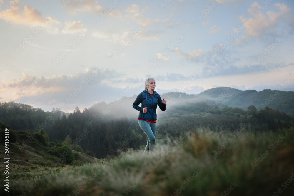 Senior woman jogging in nature on early morning with fog and mountains in background.
