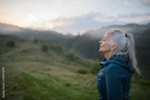 Senior woman doing breathing exercise in nature on early morning with fog and mountains in background. photo