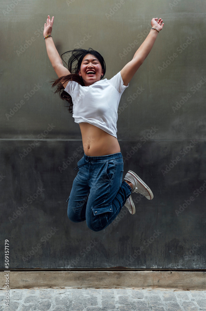 Young beautiful asian woman jumping smiling in the street