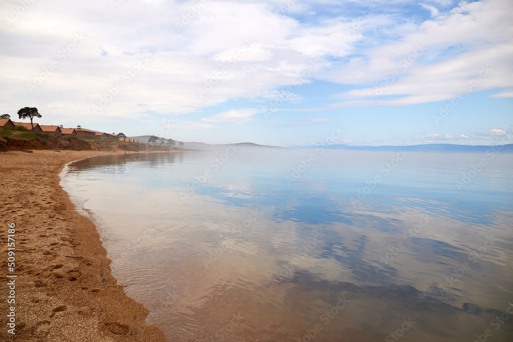 Beautiful view of Lake Baikal on a summer day. The clear calm surface of the lake, in which the clouds are reflected. The sandy shore of Olkhon Island. 