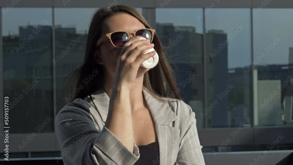 Smiling young woman in sunglasses drinks coffee from a disposable cup. Smiling young woman in sunglasses drinks coffee from a disposable cup.