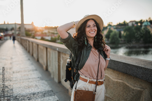 Canvas Print Young beautiful female traveler with backpack walking through bridge on sunny day in city