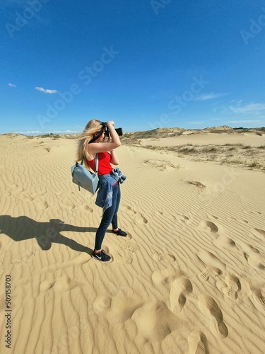 Lady photographer in a red T-shirt and jeans in a desert shooting a nature , hot summer weather outside. Leisure and sport concept