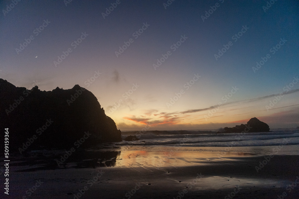 Bright orange clouds lit by the setting sun are relected in the retreating waters at Pfeiffer Beach.
