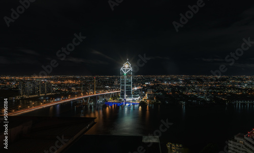 Bangkok, thailand - May 20, 2022 : Beautiful skyscrapers view and the Bridge crosses the Chao Phraya river of Bangkok city with bright glowing lights in the night. Selective focus.