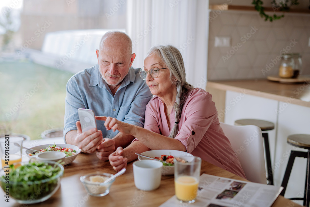 Happy senior couple using smartphone during eating dinner together at home. Happy senior couple using smartphone during eating dinner together at home.