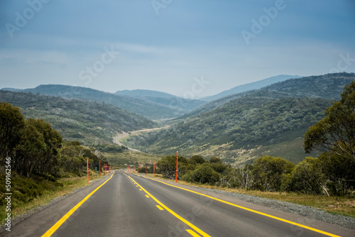 Open empty road surrounded by the mountains. Mountain winging road with high visible yellow lines. Snowy Mountains, New South Wales, Australia