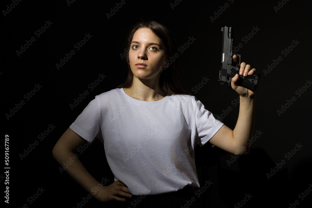 young woman with long hair in a white t-shirt holding a gun in her hand on a black background young woman with long hair in a white t-shirt holding a gun in her hand on a black background