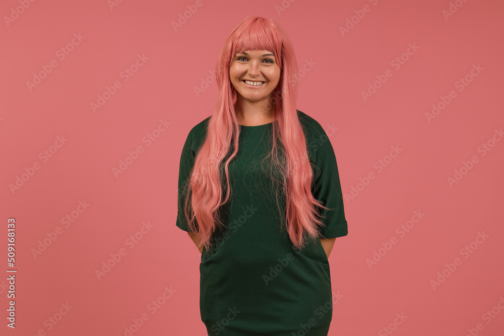 smiling young woman with long pink hair and green dress stands on a pink background smiling young woman with long pink hair and green dress stands on a pink background