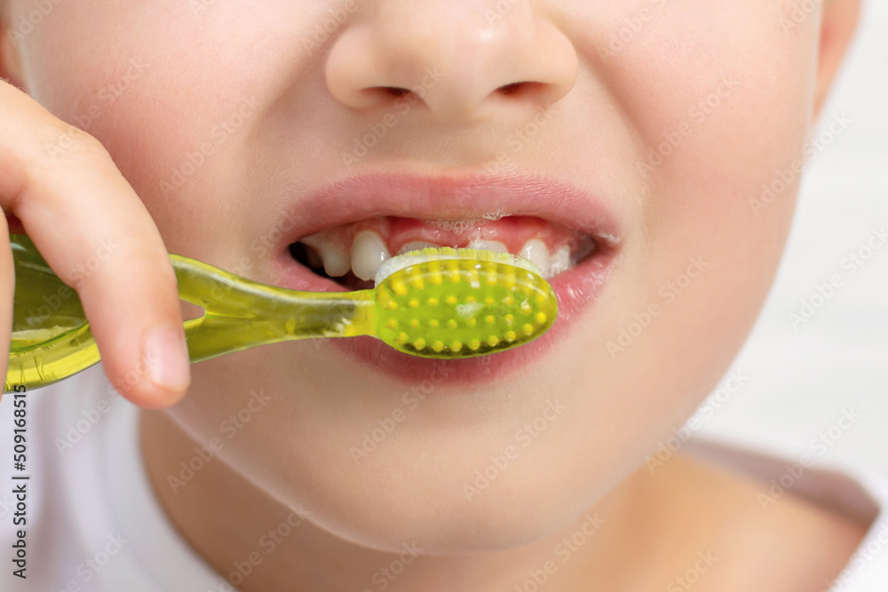 Close-up of an unrecognizable smiling child, he holds toothbrush in his hands and brushes teeth using toothpaste. Morning routine, dental hygiene after sleep. Prevention and protection against caries. Close-up of an unrecognizable smiling child, he holds toothbrush in his hands and brushes teeth using toothpaste. Morning routine, dental hygiene after sleep. Prevention and protection against caries.