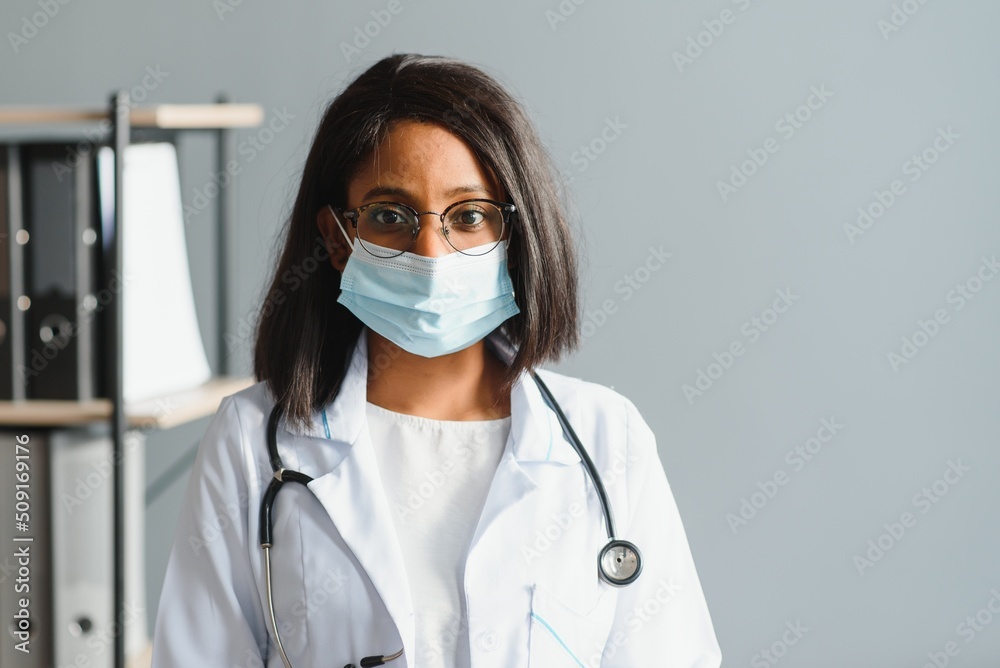 Smiling young adult indian female doctor wear white coat in medical clinic office. Happy beautiful health care india professional medic physician, therapist, headshot portrait