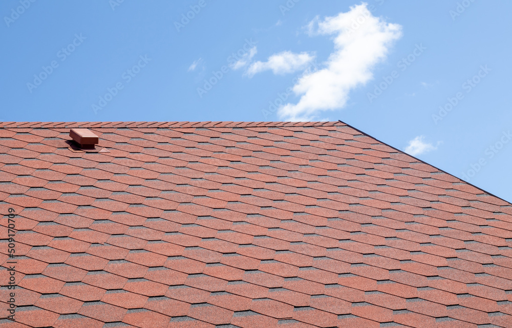 New roof with red shingles against the blue sky. High quality photo. Tiles on the roof of the house. Use to advertise roof fabrication and maintenance. Spotted texture. Affordable roofing.