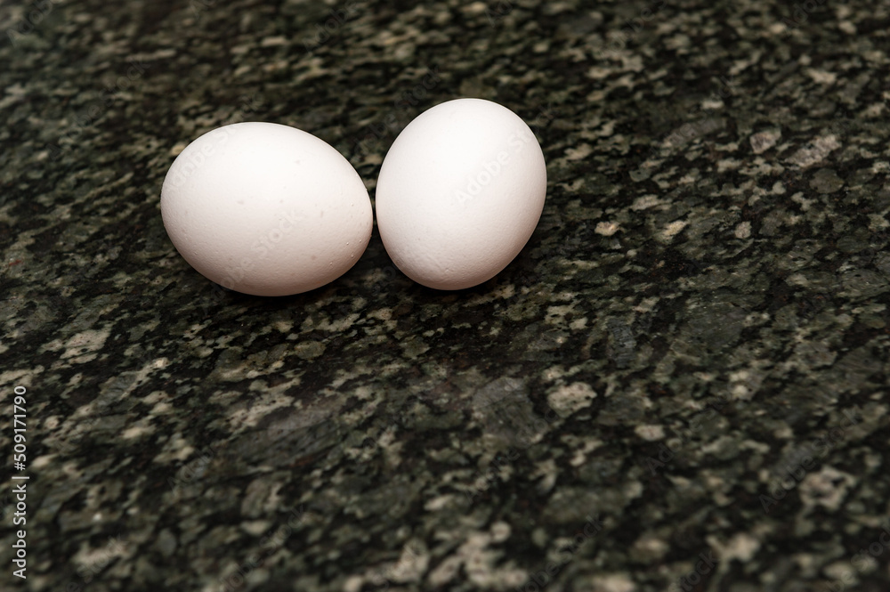 Two white chicken eggs on a granite counter with a shallow depth of field and copy space Two white chicken eggs on a granite counter with a shallow depth of field and copy space
