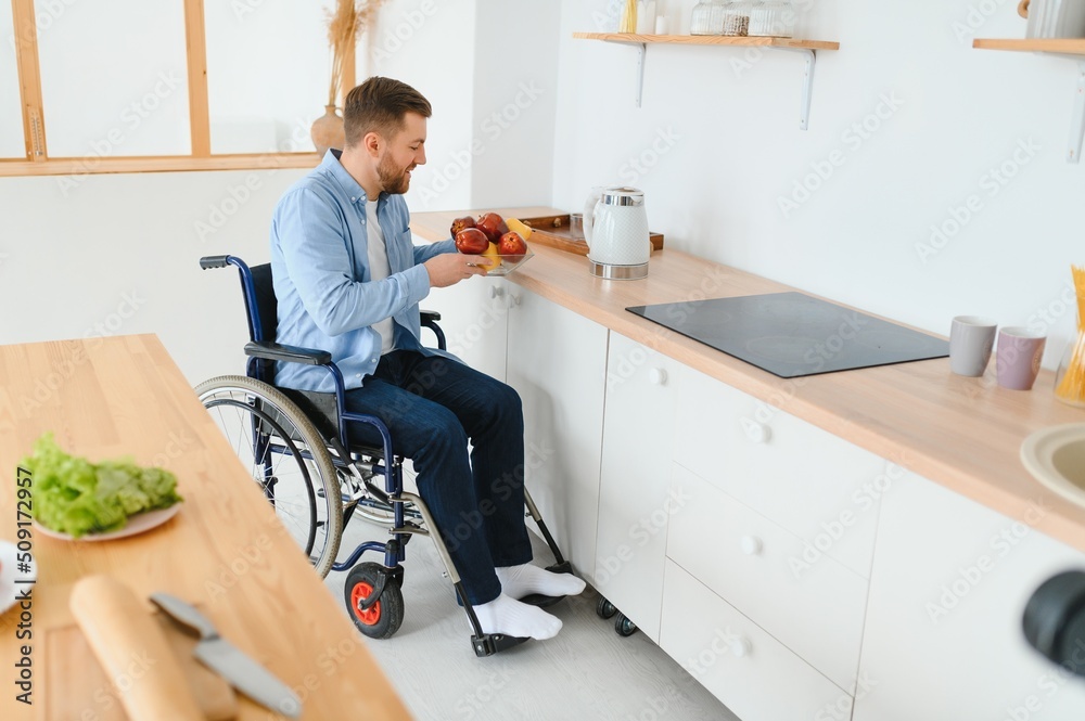 Young Disabled Man On Wheelchair In The Kitchen. Young Disabled Man On Wheelchair In The Kitchen.