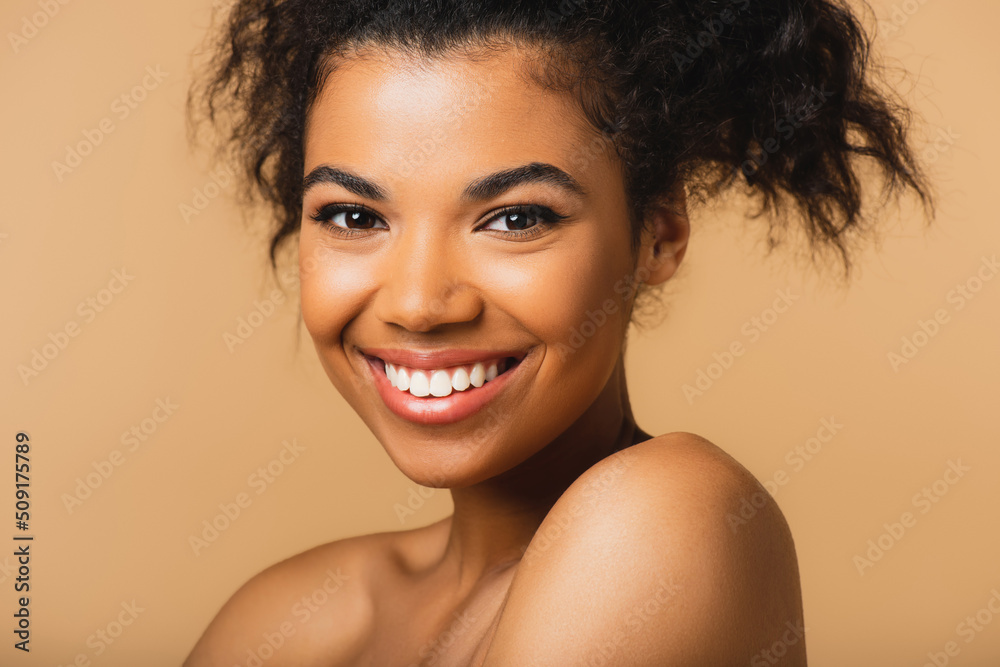 portrait of cheerful african american woman with bare shoulders and perfect skin isolated on beige. - obrazy, fototapety, plakaty 