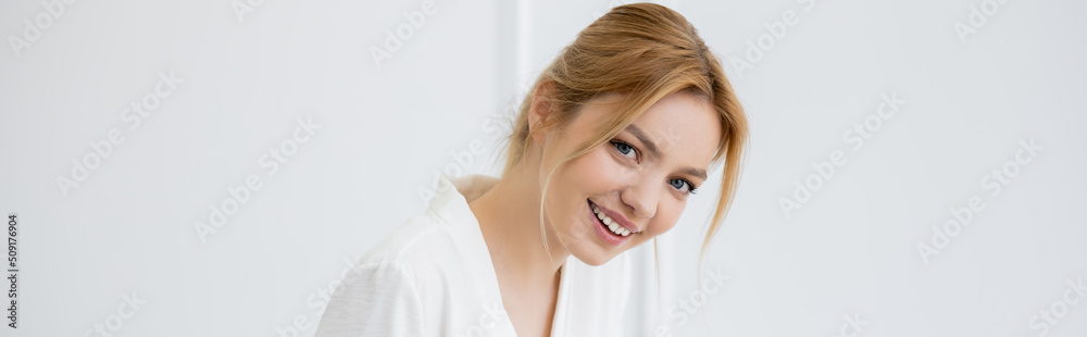 Naklejka premium Cheerful young woman in white blouse looking at camera at home, banner.