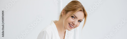 Cheerful young woman in white blouse looking at camera at home, banner.