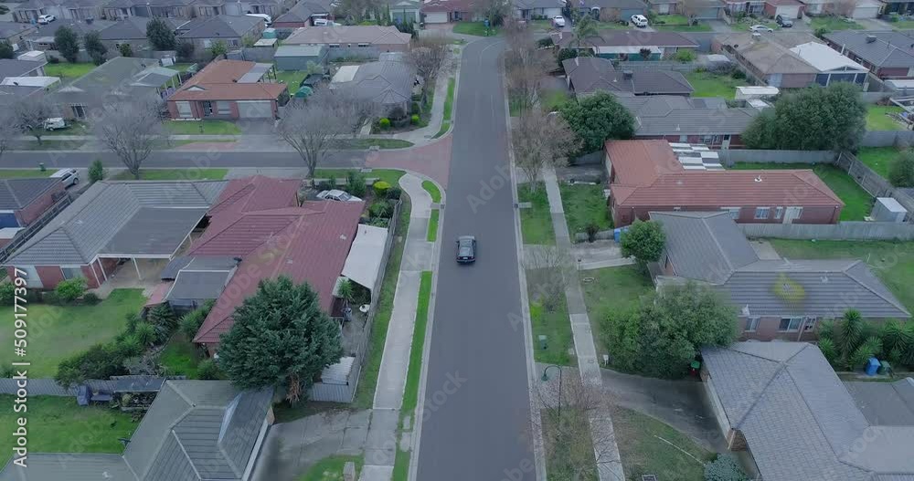 Aerial shot of car driving in the street between houses or colony. Aerial. 4K. Drone moves along the street between houses . Red roofs surround the road. Aerial shot of car driving in the street between houses or colony. Aerial. 4K. Drone moves along the street between houses . Red roofs surround the road.