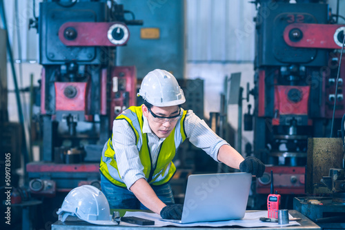 The white safety helmet working with laptop in front of machinery