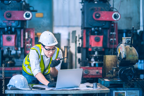 The white safety helmet working with laptop and order thought a walkie talkie in front of machinery