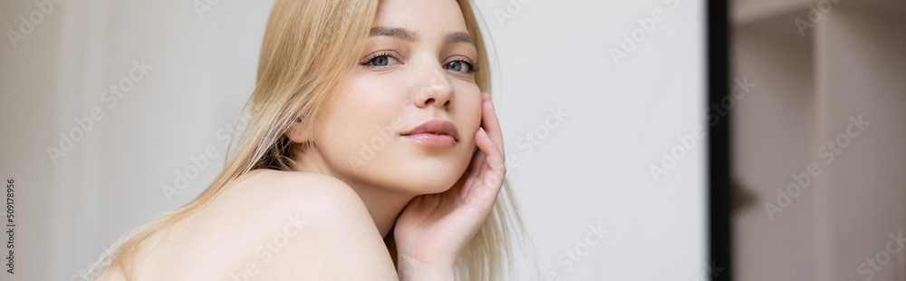 Young blonde woman with naked shoulder looking at camera at home, banner. Young blonde woman with naked shoulder looking at camera at home, banner.