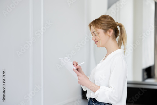 Side view of happy woman in blouse writing on notebook in living room.