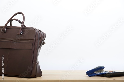 A business leather briefcase stands next to an accounting calculator and a stapler.