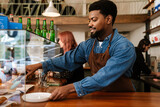 Black bearded man wearing apron smiling while working in cafe