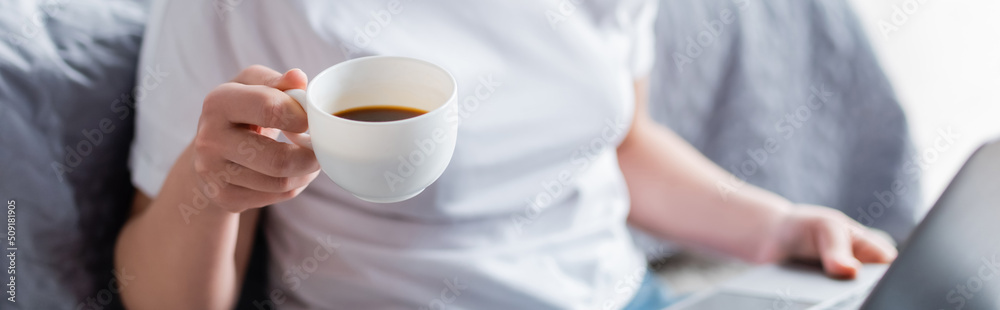partial view of blurred woman holding cup of coffee at home, banner. partial view of blurred woman holding cup of coffee at home, banner.
