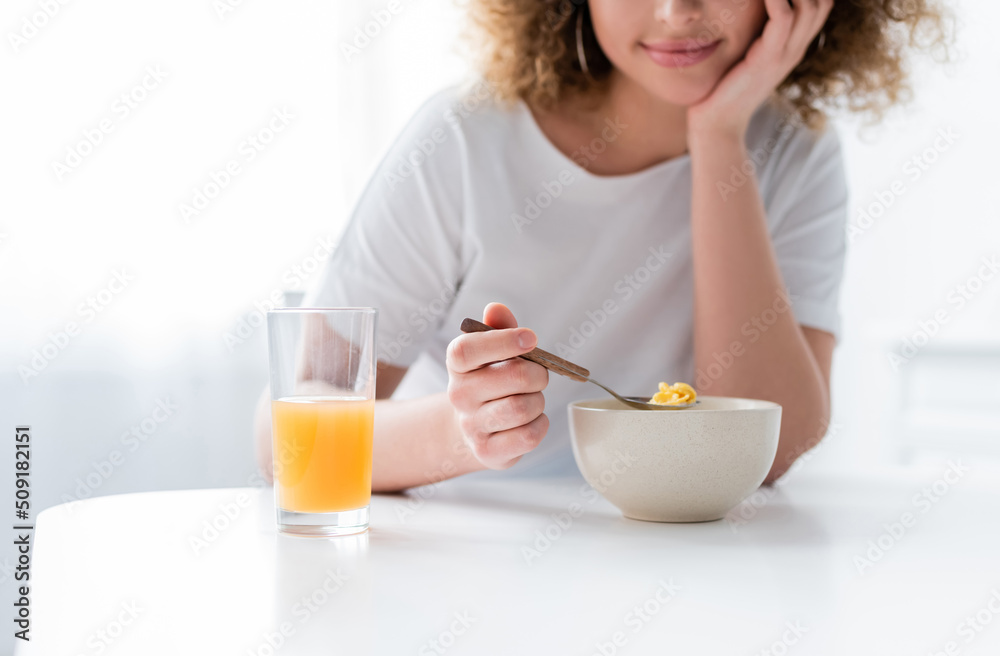 cropped view of smiling woman holding spoon with corn flakes near bowl and glass of orange juice. cropped view of smiling woman holding spoon with corn flakes near bowl and glass of orange juice.