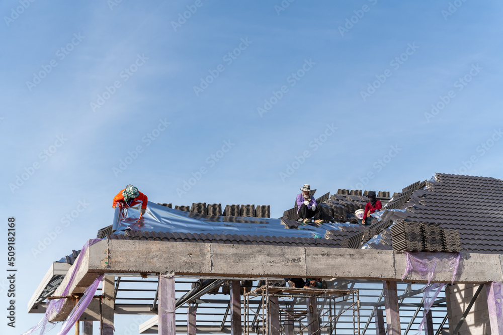 Naklejka premium Roofers is installing insulating sheets on a concrete tile roof.