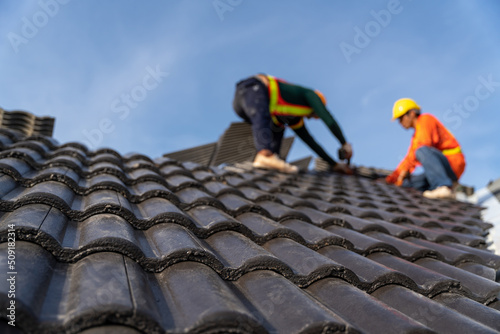 2 roofers working on the working at height to install the Concrete Roof Tiles on the new roof of new modern building construction. Selective focus of Concrete Roof Tiles.