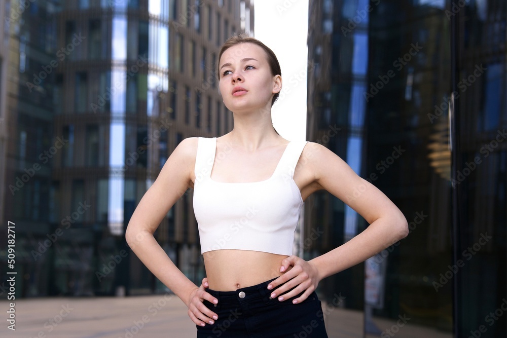 Portrait of beautiful teen teenager young slim fit athletic girl in a good shape. Attractive pretty woman standing outdoors at summer day looking at camera in top T-shirt in the city Portrait of beautiful teen teenager young slim fit athletic girl in a good shape. Attractive pretty woman standing outdoors at summer day looking at camera in top T-shirt in the city