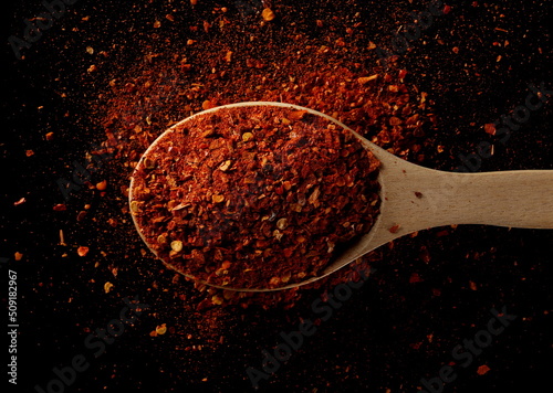 Foto Spicy chili pepper flakes, crushed, milled dry paprika pile in wooden spoon isol